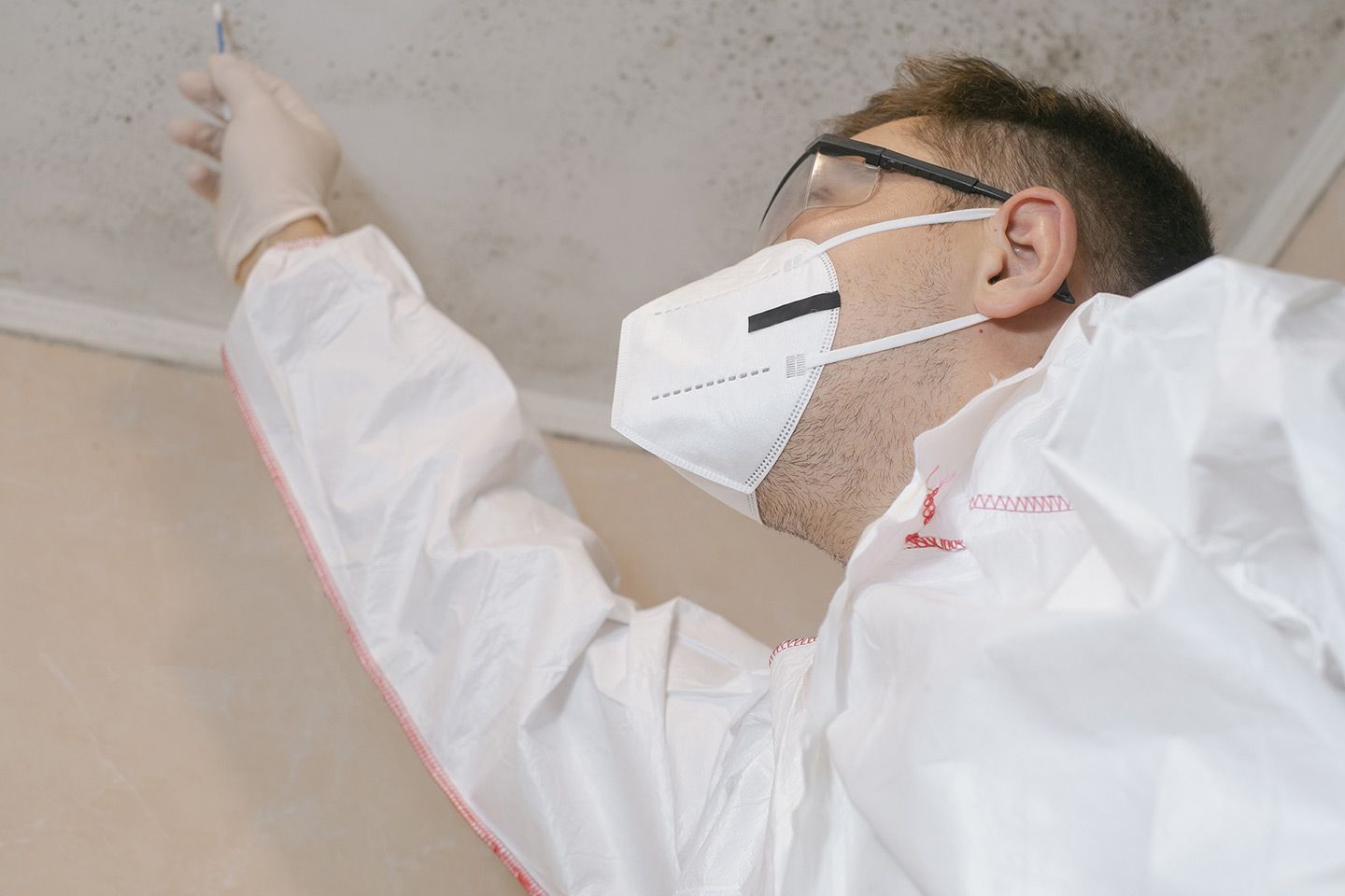 Person in protective suit inspecting ceiling for mold.