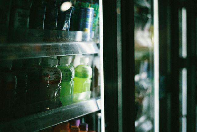 Refrigerated shelf with assorted bottled drinks, including green and dark cans and bottles.