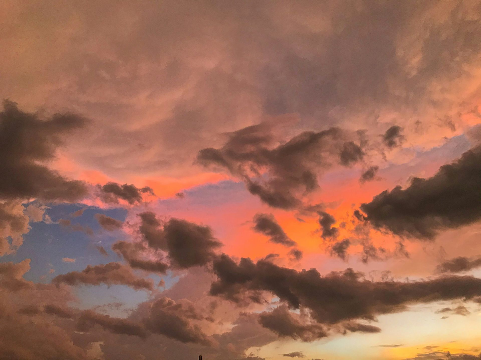 Vivid sunset sky with silhouetted clouds painted in striking shades of orange and pink.
