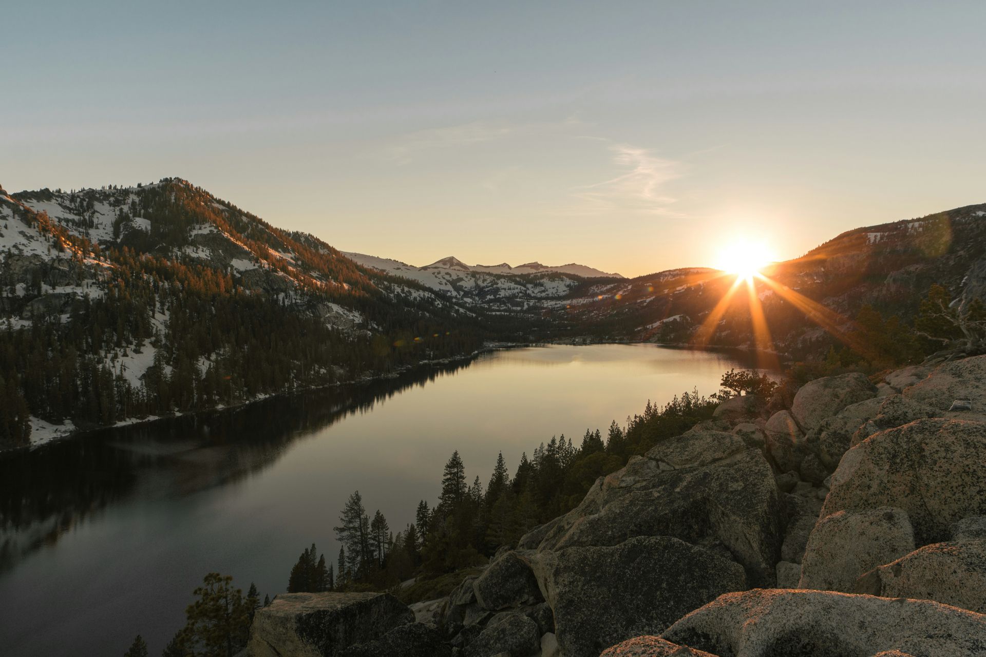 Sunshine peeking over mountains with a still lake