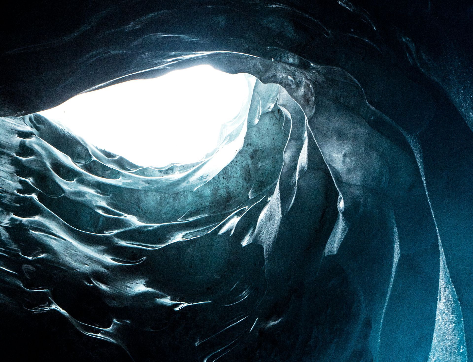 A glacial ice cave with textured walls and an opening showing light.