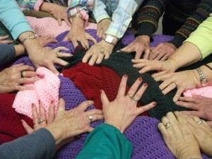 Hands reach into a pile of colorful crocheted blankets.
