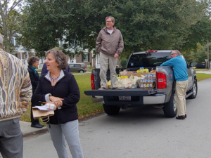 People unloading groceries from a truck on a street.  One man stands in the truck bed; others stand nearby.