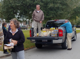 People loading food items from a truck on a street. One man stands in the truck bed, two others near the tailgate.