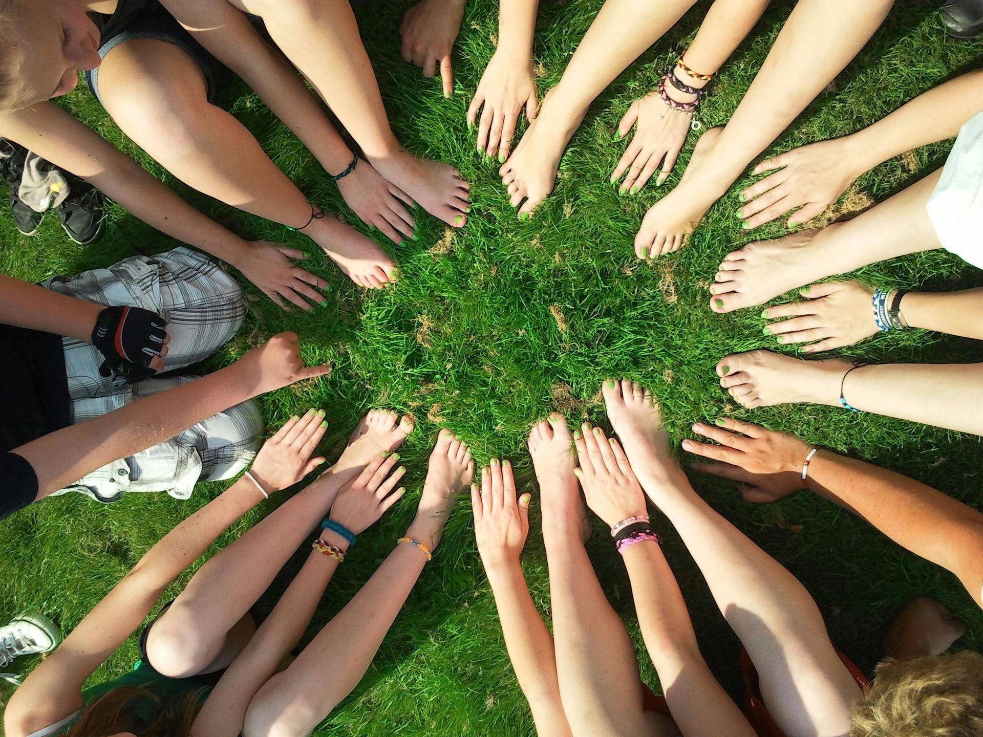Hands and bare feet of a group forming a circle on green grass.