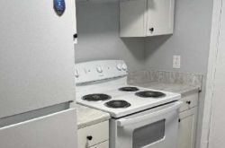White kitchen with stove, cabinets, and refrigerator. Light gray walls and countertops.
