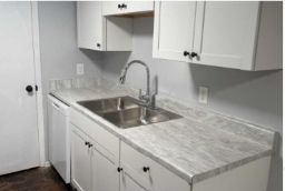 White kitchen with stainless steel sink and countertops, cabinets, and a faucet.