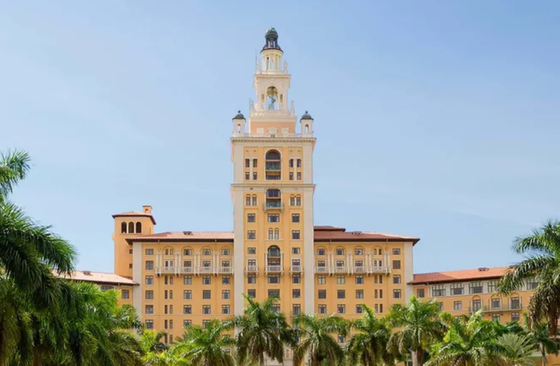 A large building with a clock tower and palm trees in front of it.