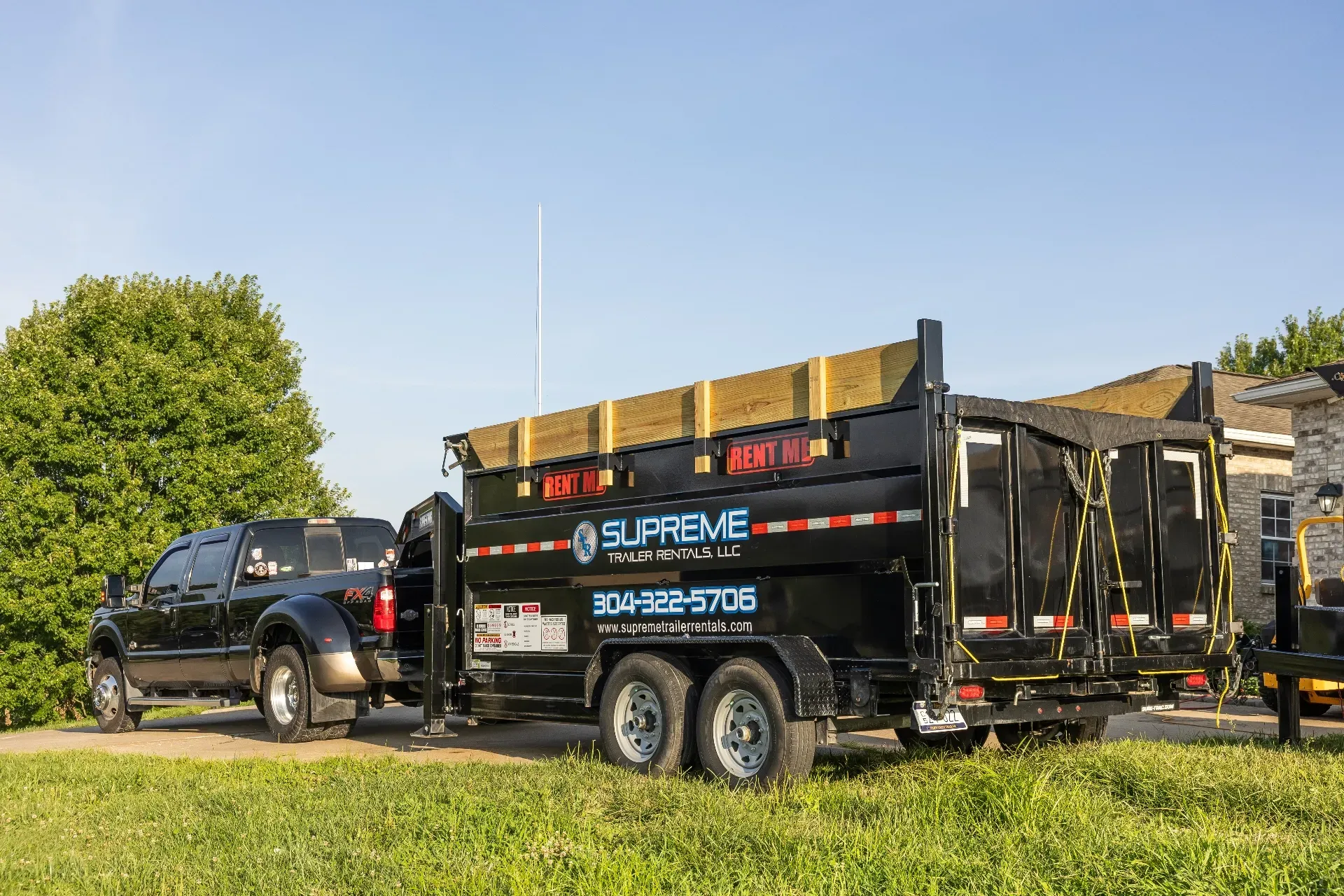 Black truck towing a black dumpster trailer; the trailer has the company name 