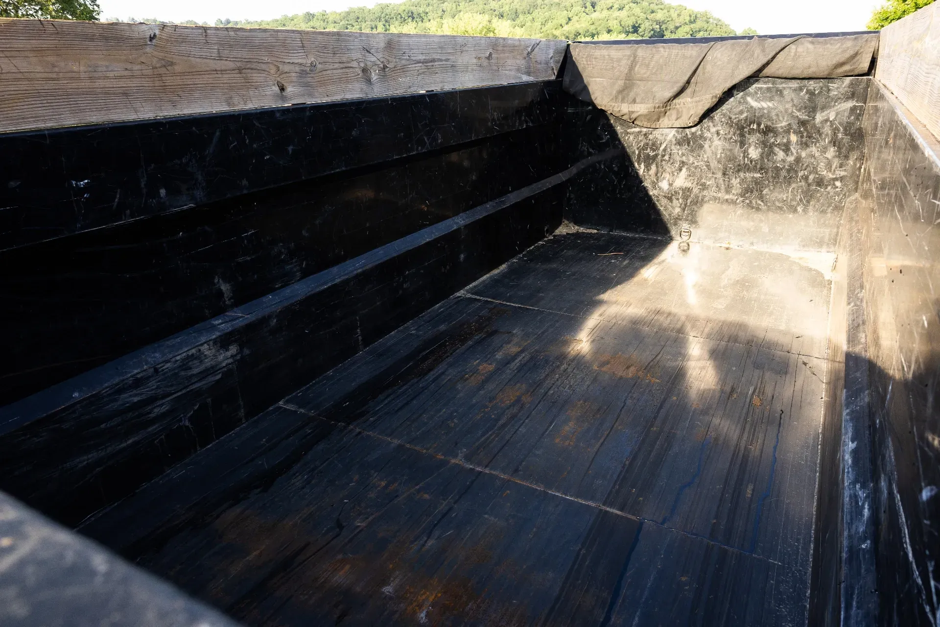 Inside view of a black, wooden box, possibly a truck bed, with a sloping front and light shining on the wooden planks.