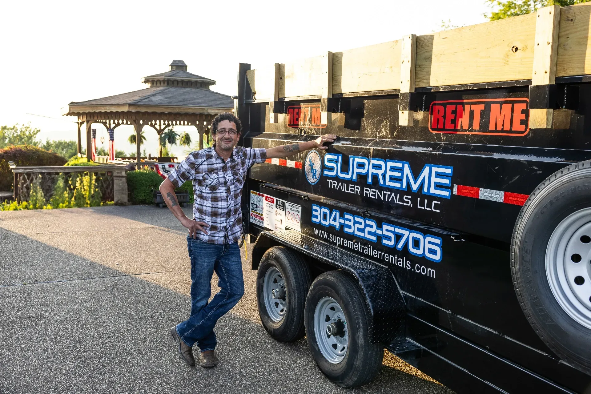 Man in plaid shirt leans against a black trailer with 