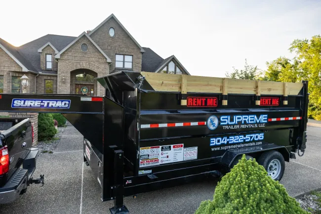 Black Supreme Trailer Rental trailer parked in a driveway in front of a brick house.