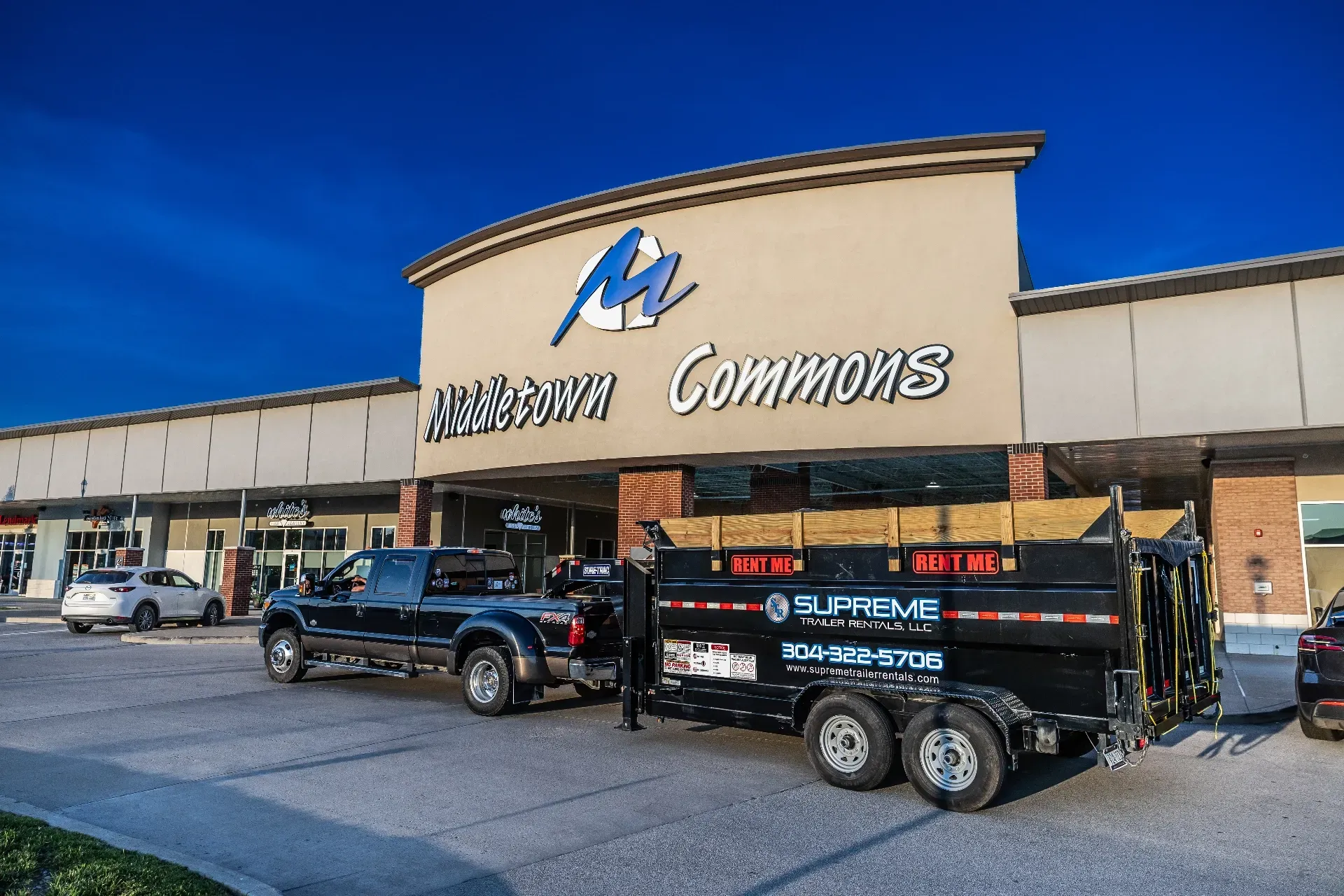 A black pickup truck towing a loaded trailer in front of the Aurora Commons shopping center.