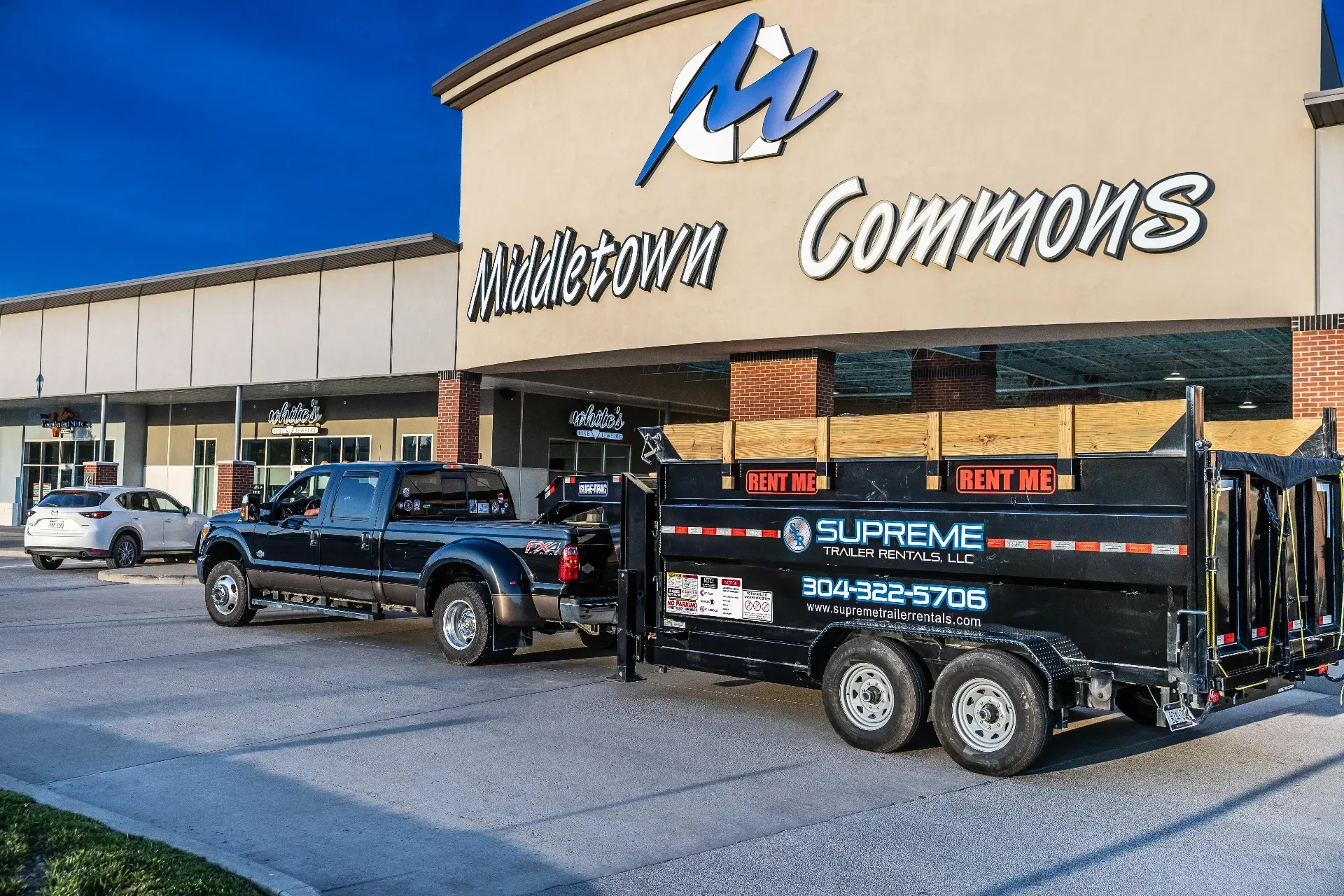 A black pickup truck with a trailer in front of a shopping center. The trailer has the
