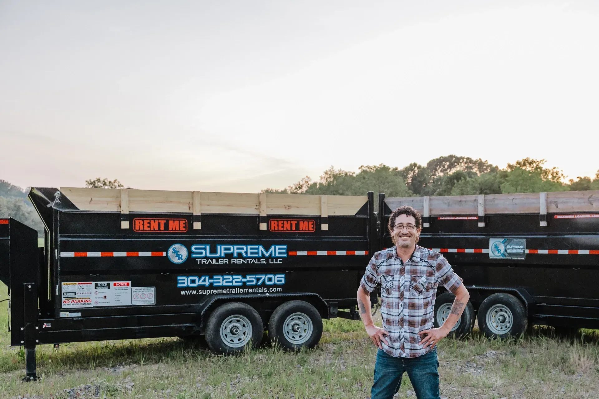 Man with hands on hips poses next to a black Supreme Roll-Off trailer in an outdoor setting.