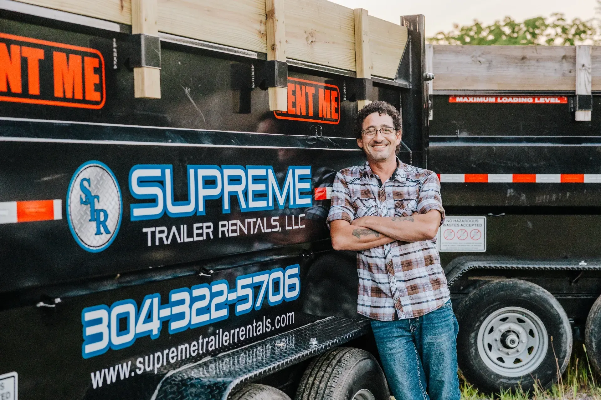 Man with crossed arms stands by a black trailer with