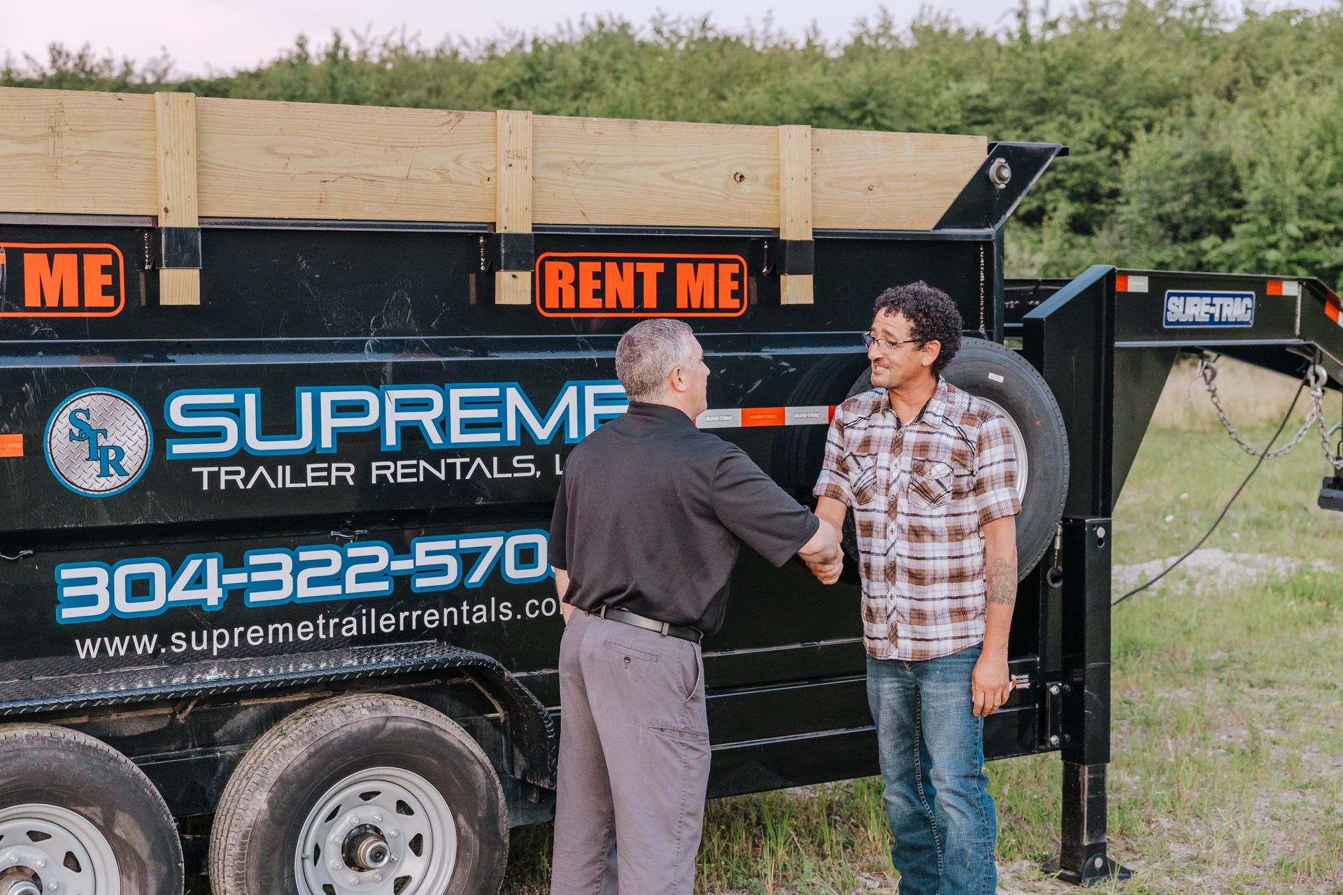 Two men shaking hands in front of a black trailer. The trailer has 