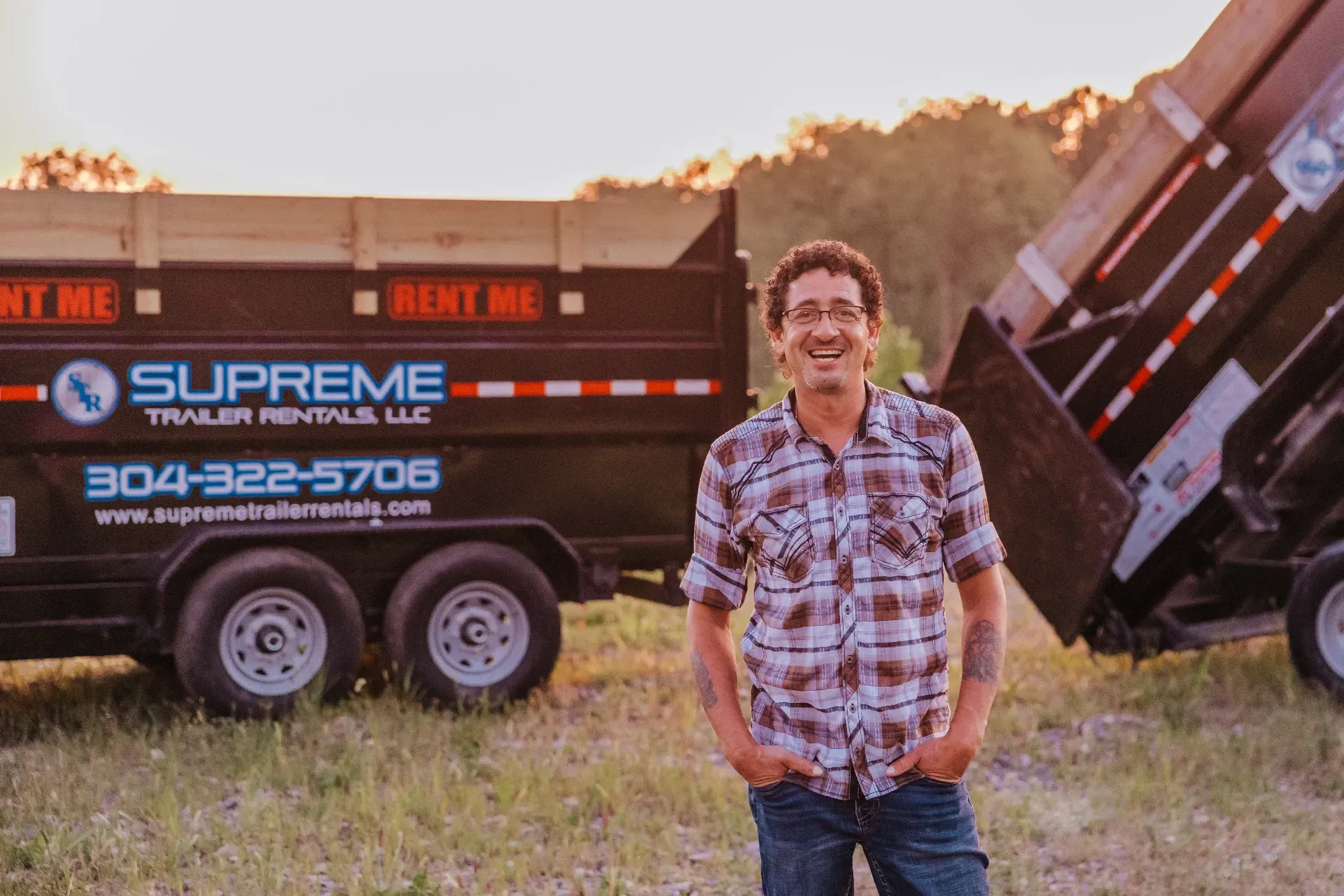 Man standing in field, smiling in front of a black trailer. The trailer has