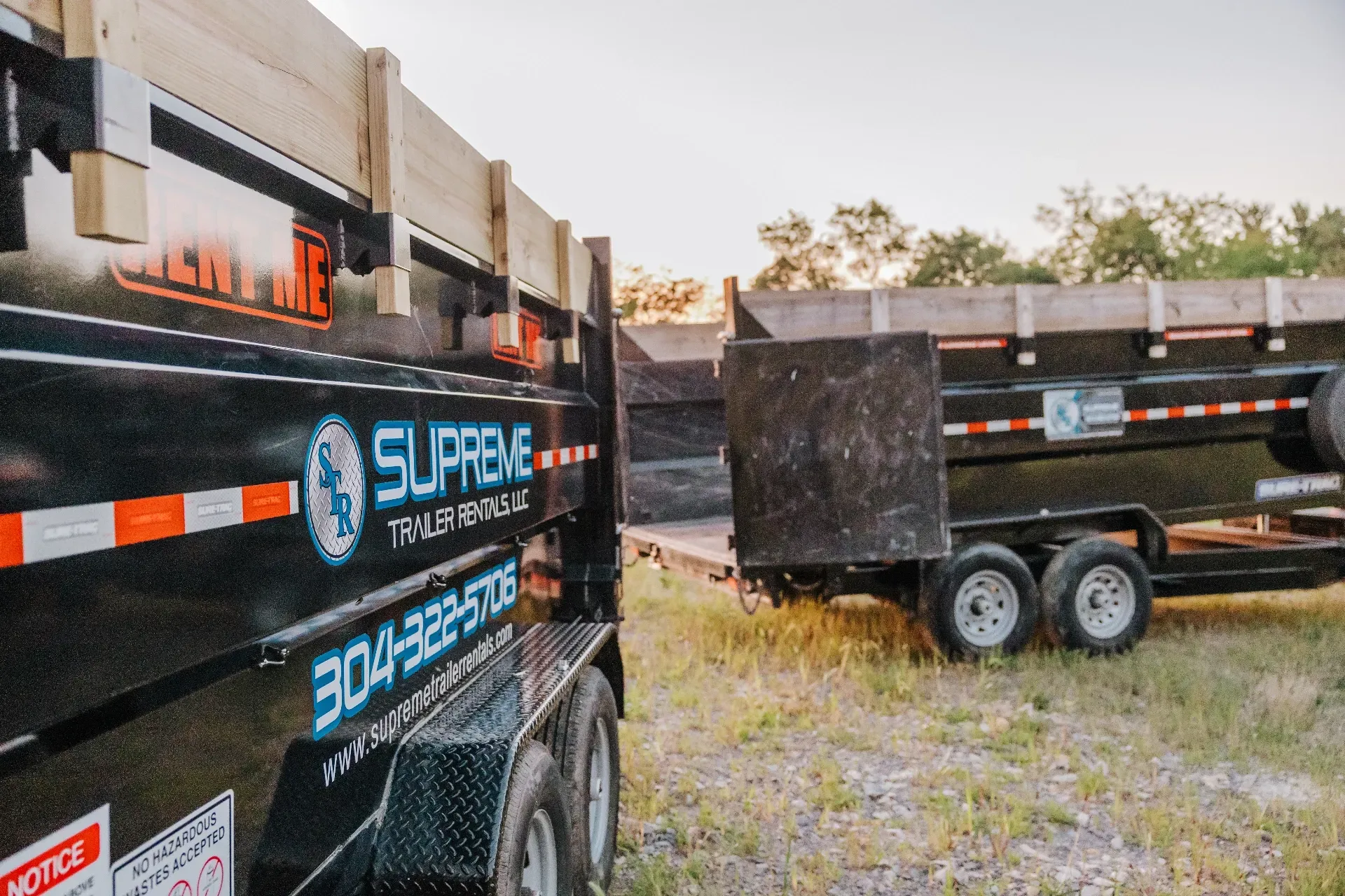 Two black dump trailers with wooden sides parked outdoors. The closer trailer has 