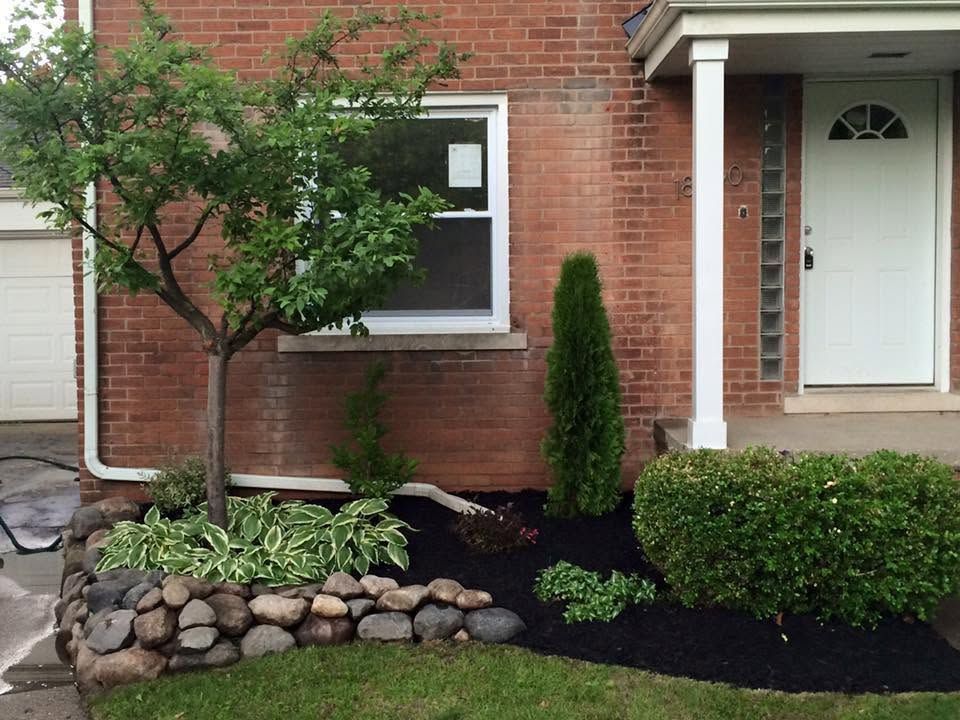 Brick house front entrance with landscaped garden, stone border, shrubs, and small tree.