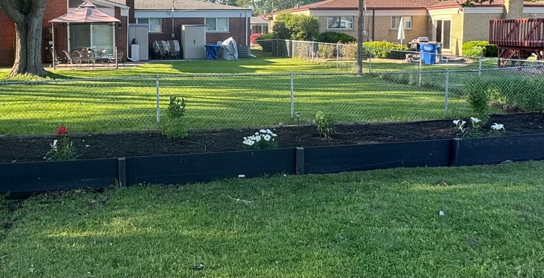 Backyard garden with black retaining wall, green grass, and houses in the background