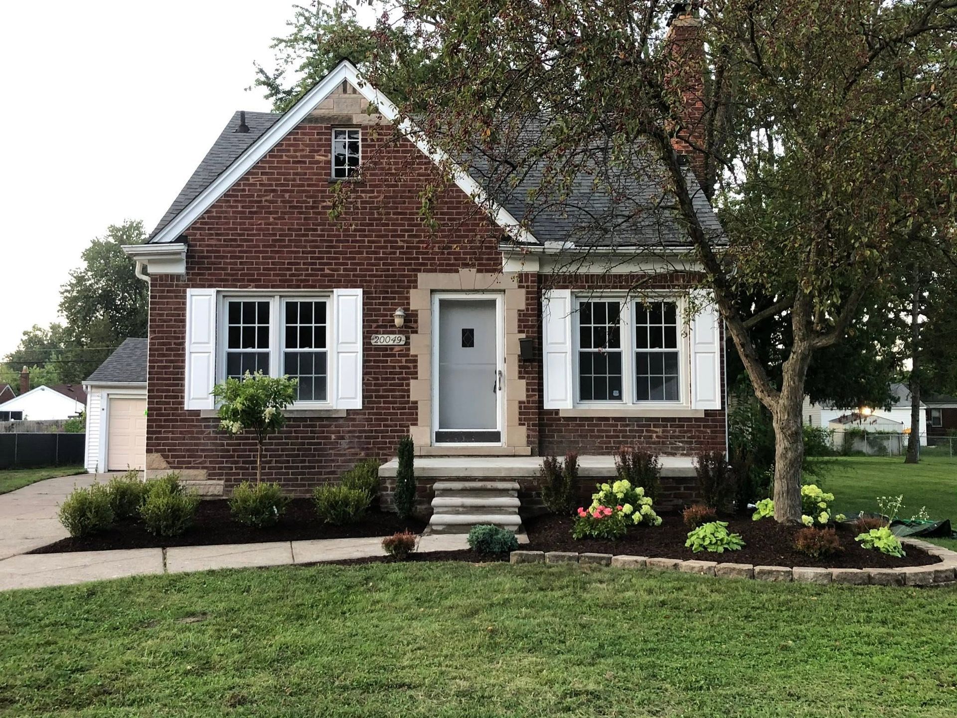 Brick house with white trim, front steps, and landscaped yard under trees