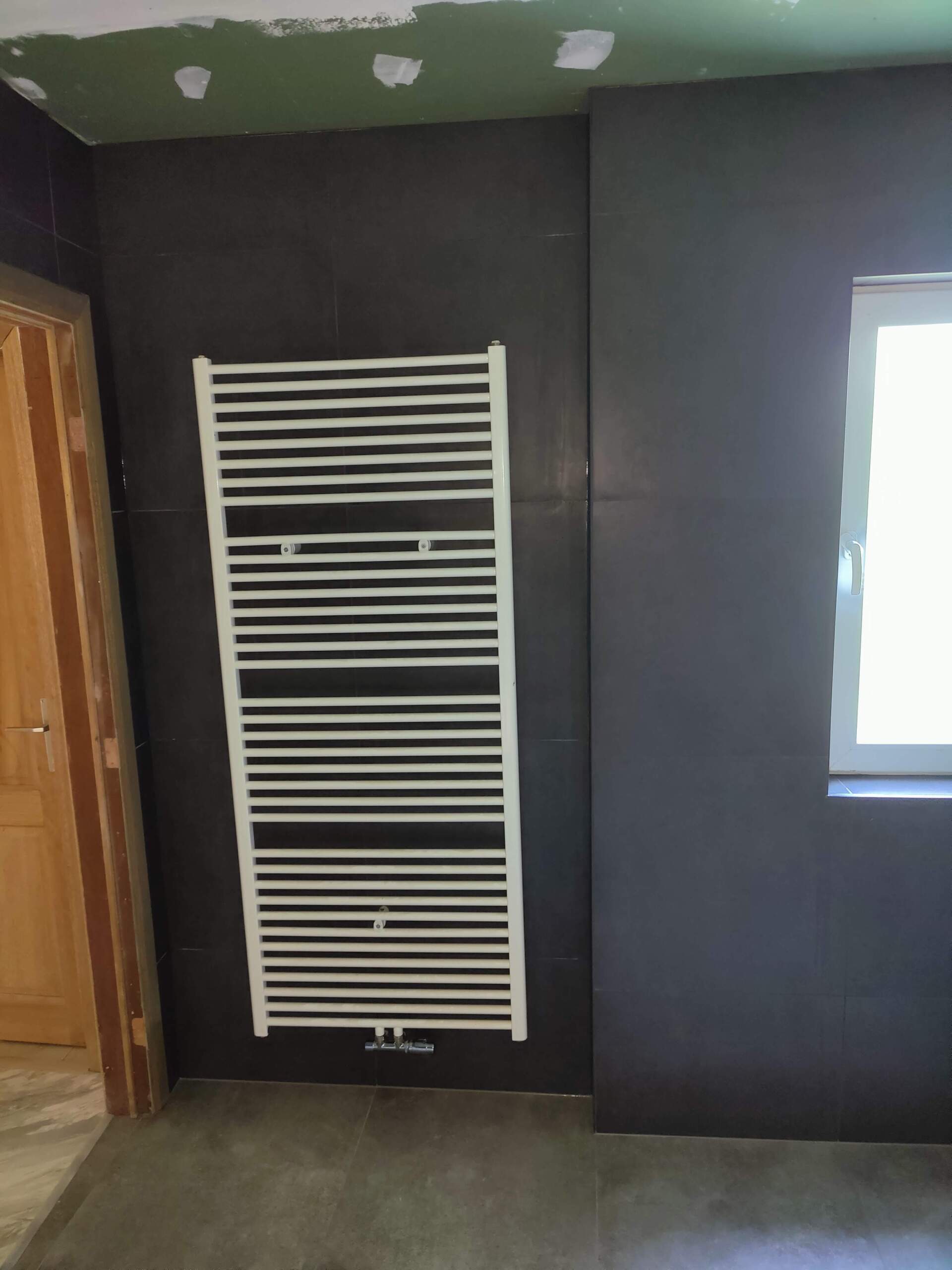 A white towel rack is hanging on a black wall next to a window