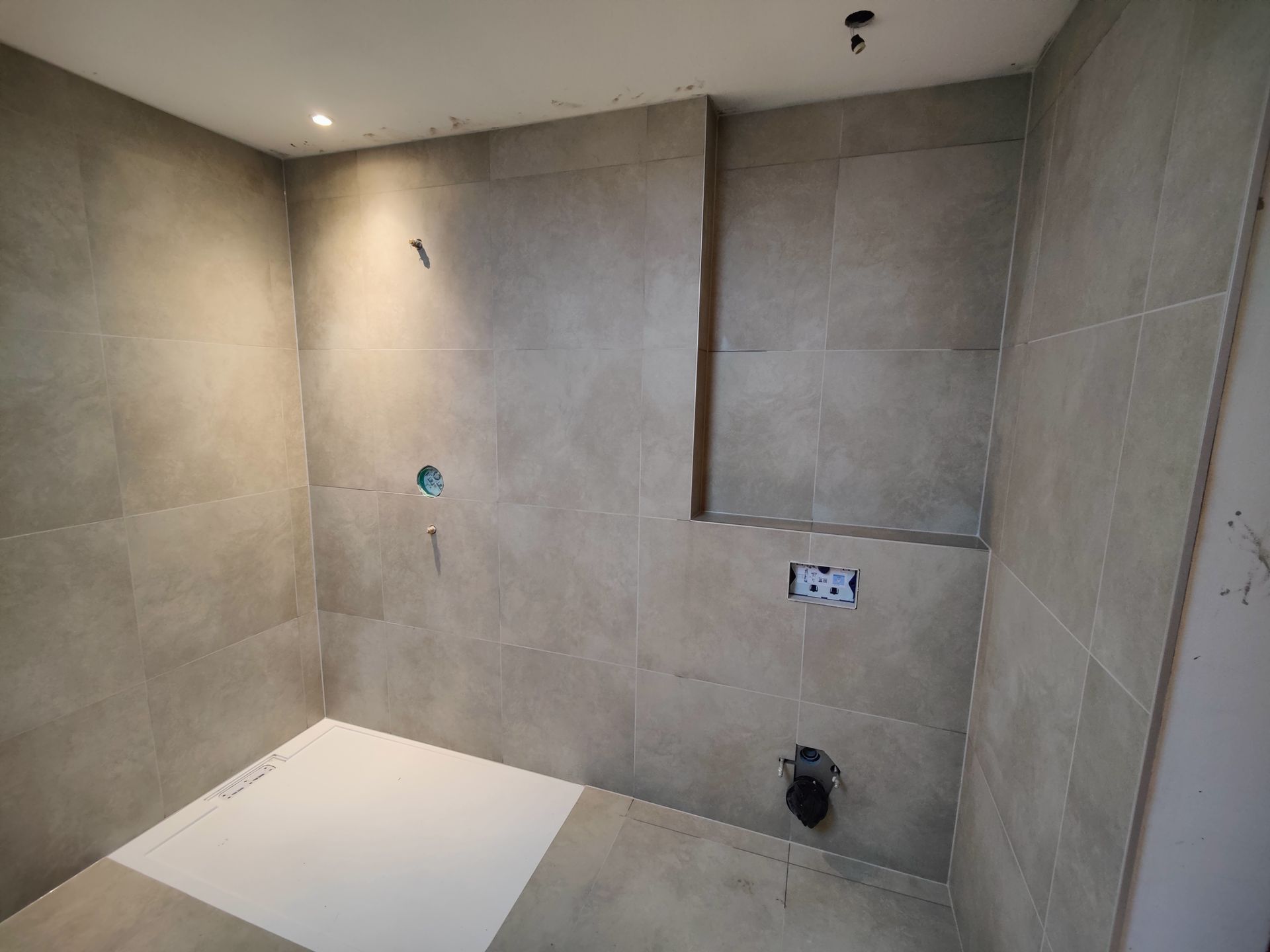 A bathroom with gray tiles and a white shower stall.