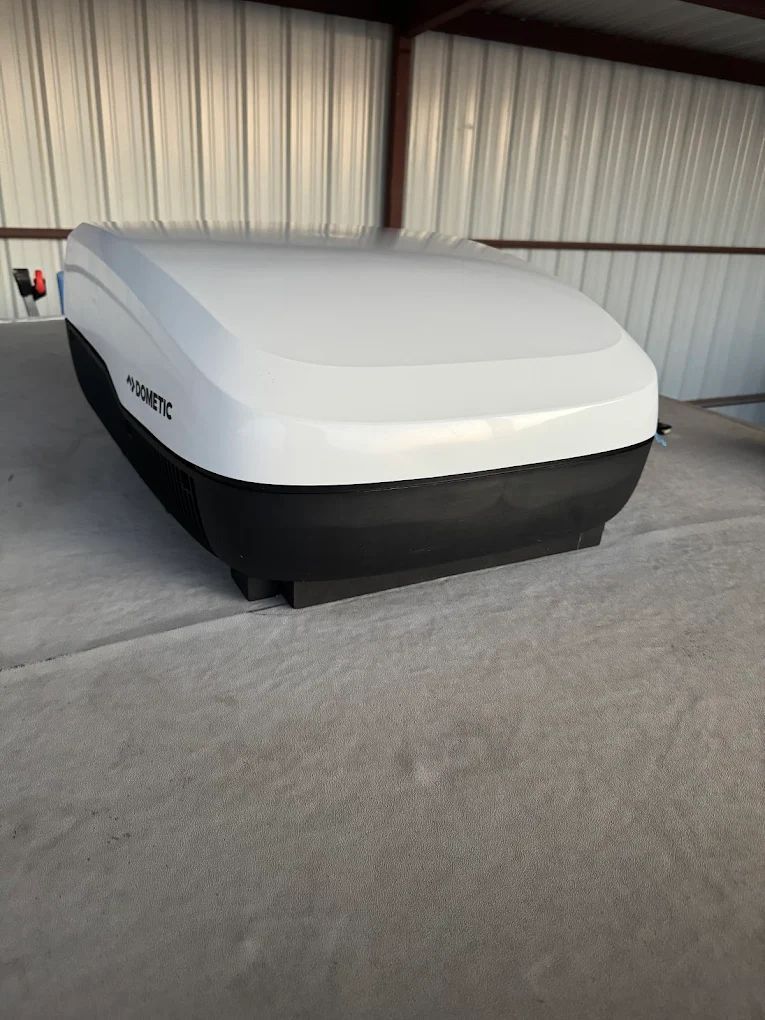 A white and black Dometic roof-mounted cargo box on a vehicle roof under a metal shelter.