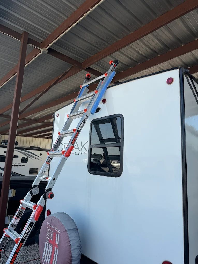 Ladder leaning against a white RV, reaching up to the metal roof of a carport.