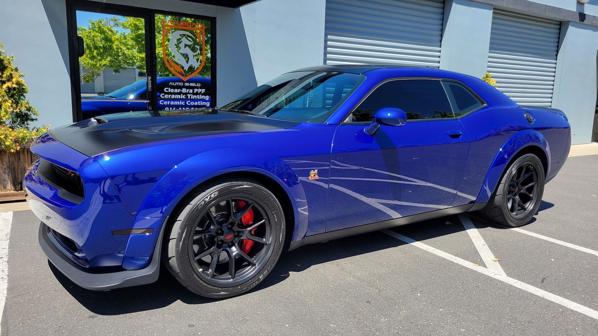 A blue dodge challenger is parked in a parking lot in front of a building.