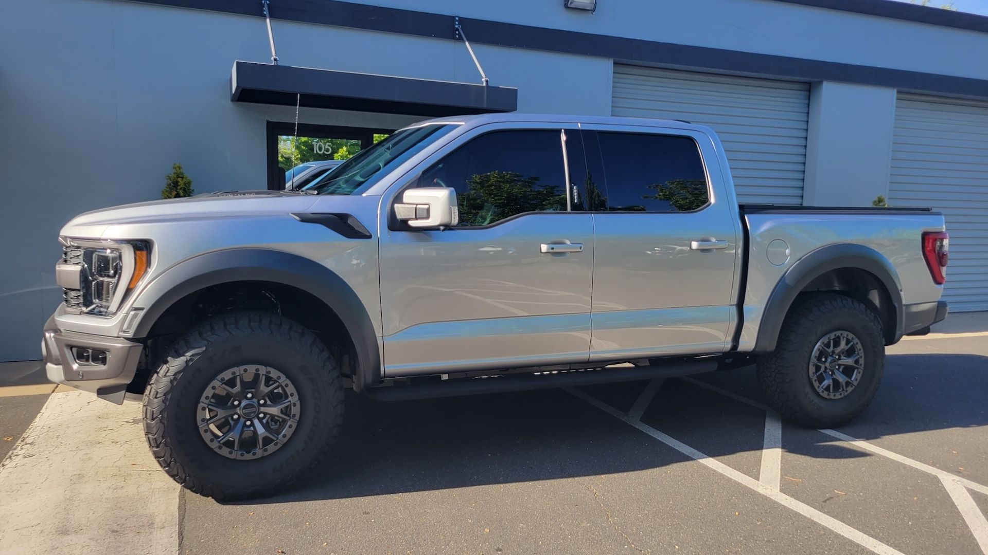 A silver pickup truck is parked in a parking lot in front of a building.