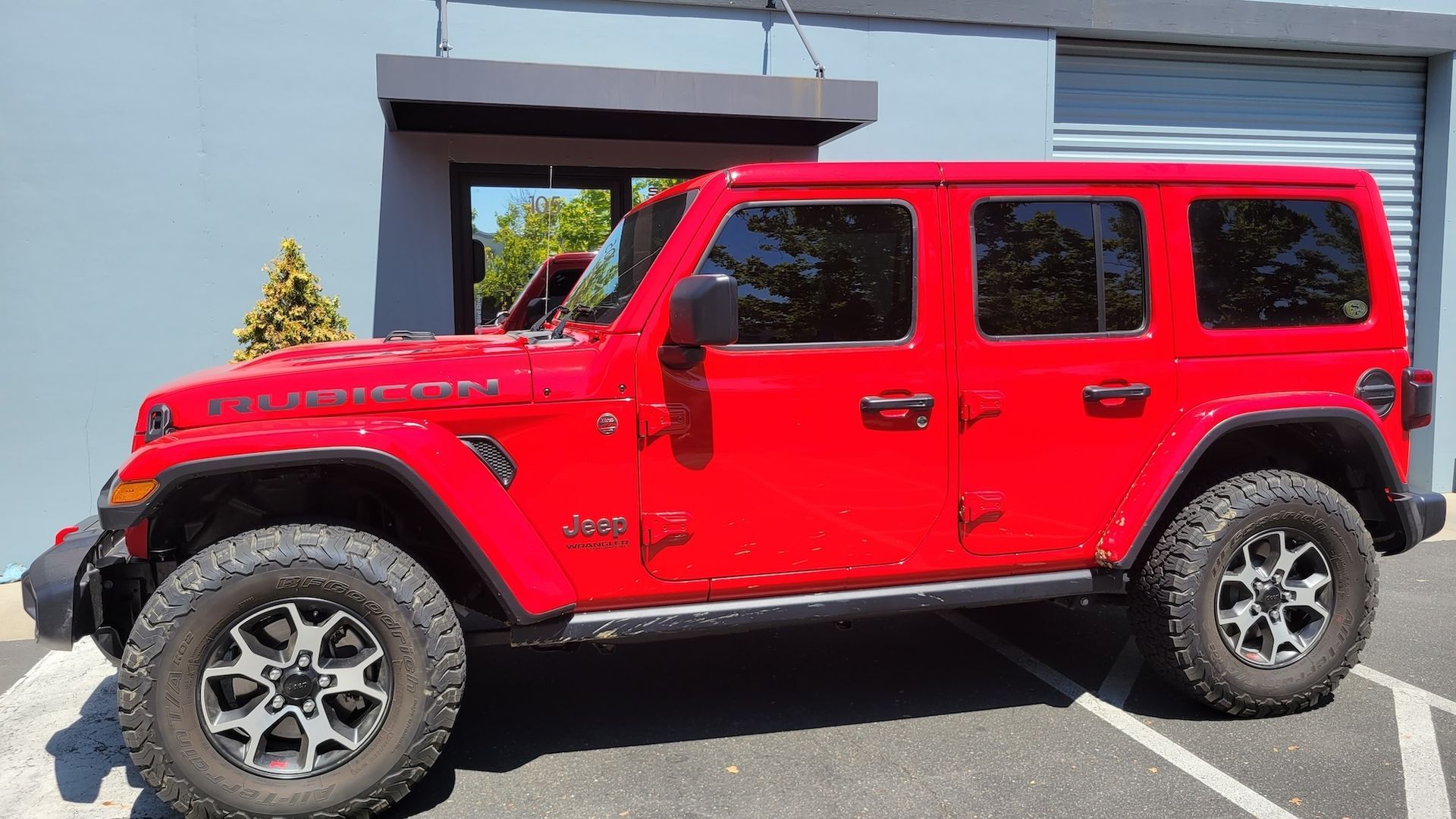 A red jeep wrangler is parked in front of a building.
