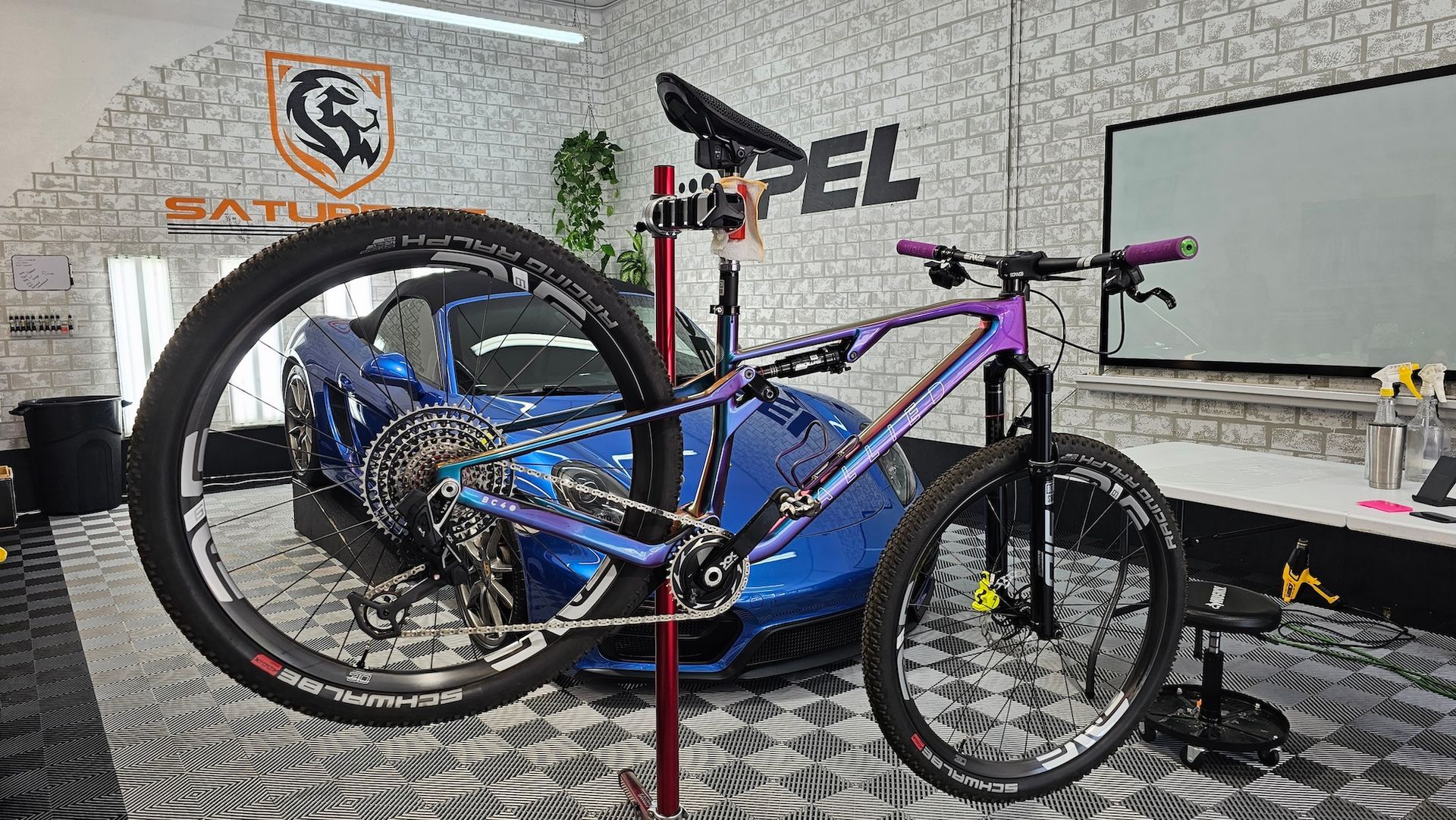 A bicycle is sitting on a stand in a garage next to a blue car.