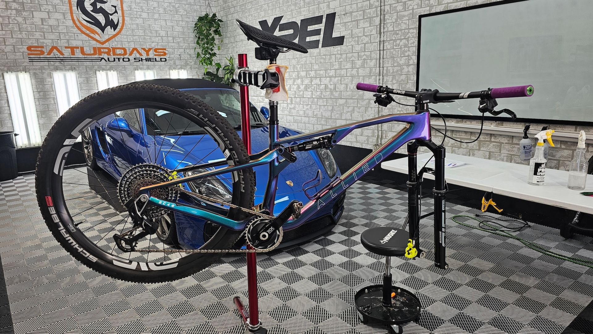 A bicycle is sitting on a stand in a garage next to a blue car.