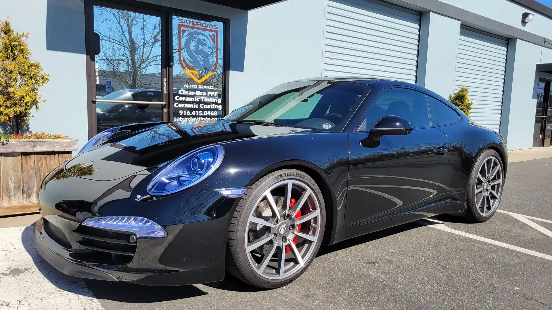 A black porsche 911 is parked in a parking lot in front of a building.
