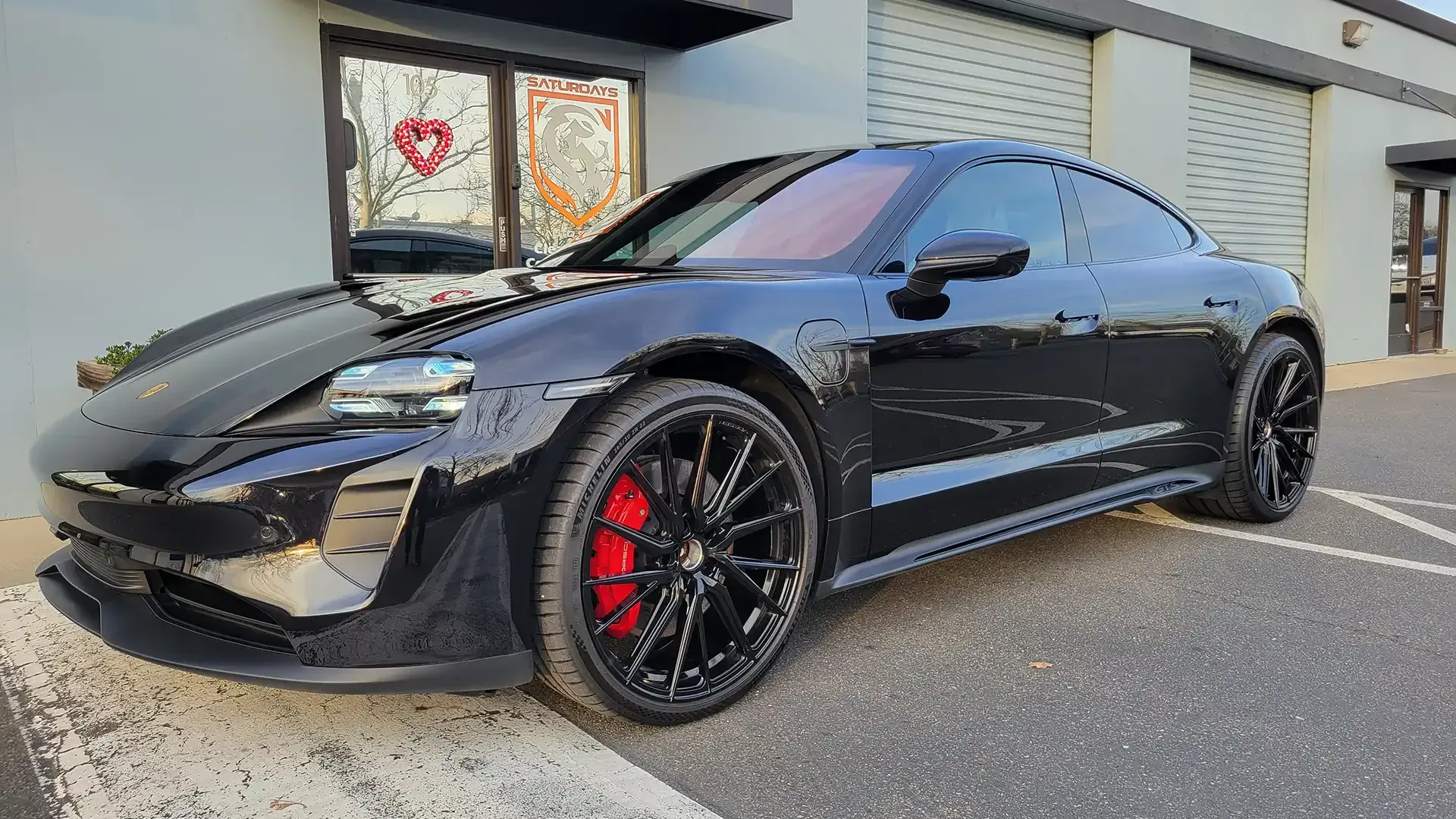 A black porsche taycan is parked in front of a building.