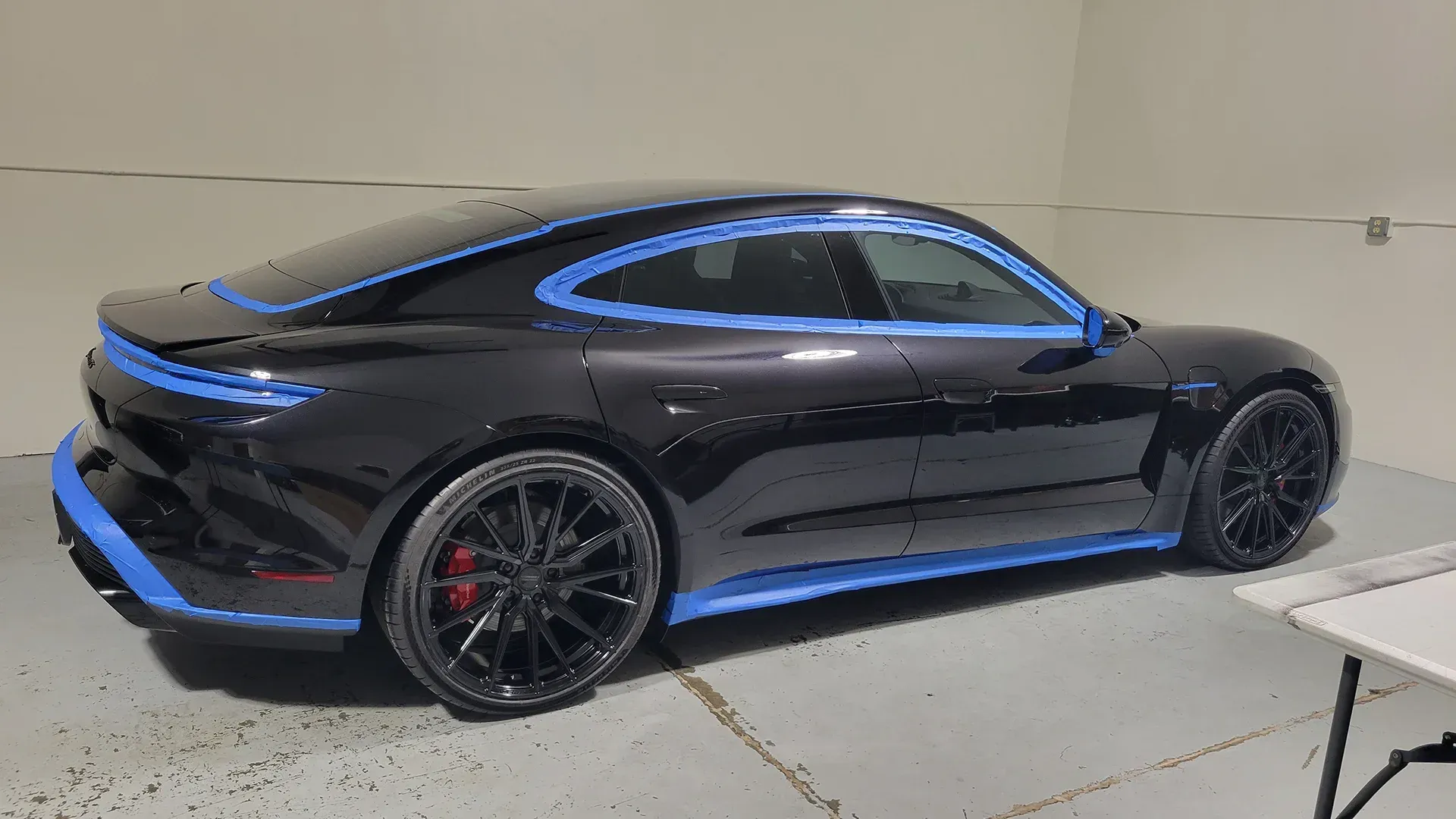 A black porsche taycan is sitting on a table in a garage.