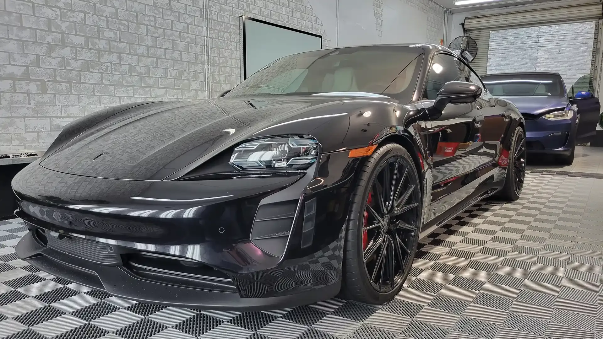 A black porsche taycan is parked in a garage.