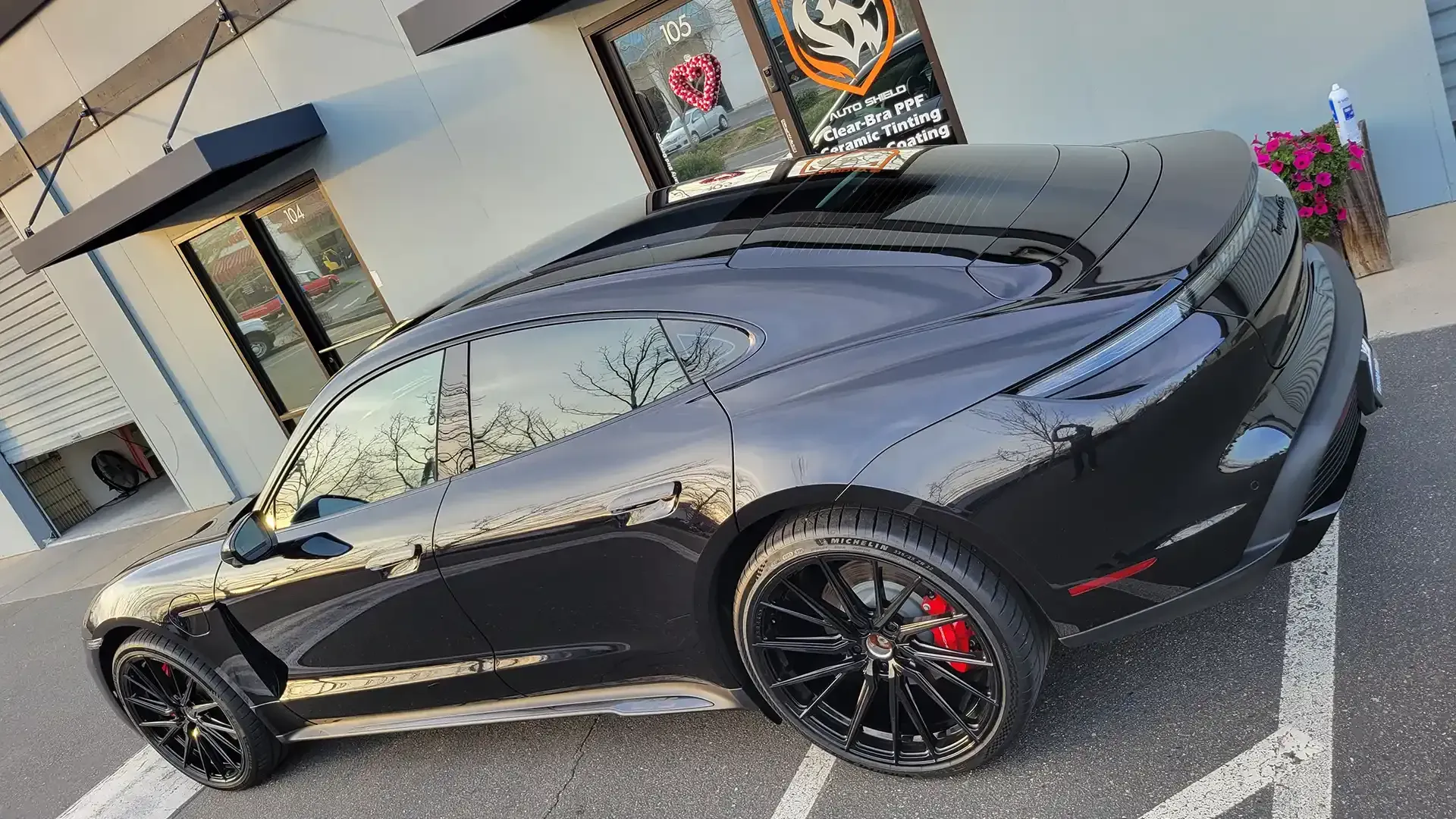 A black porsche taycan is parked in a parking lot in front of a building.