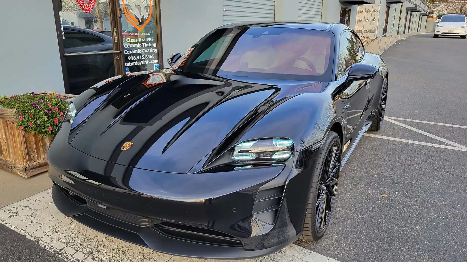 A black porsche taycan is parked in a parking lot in front of a building.