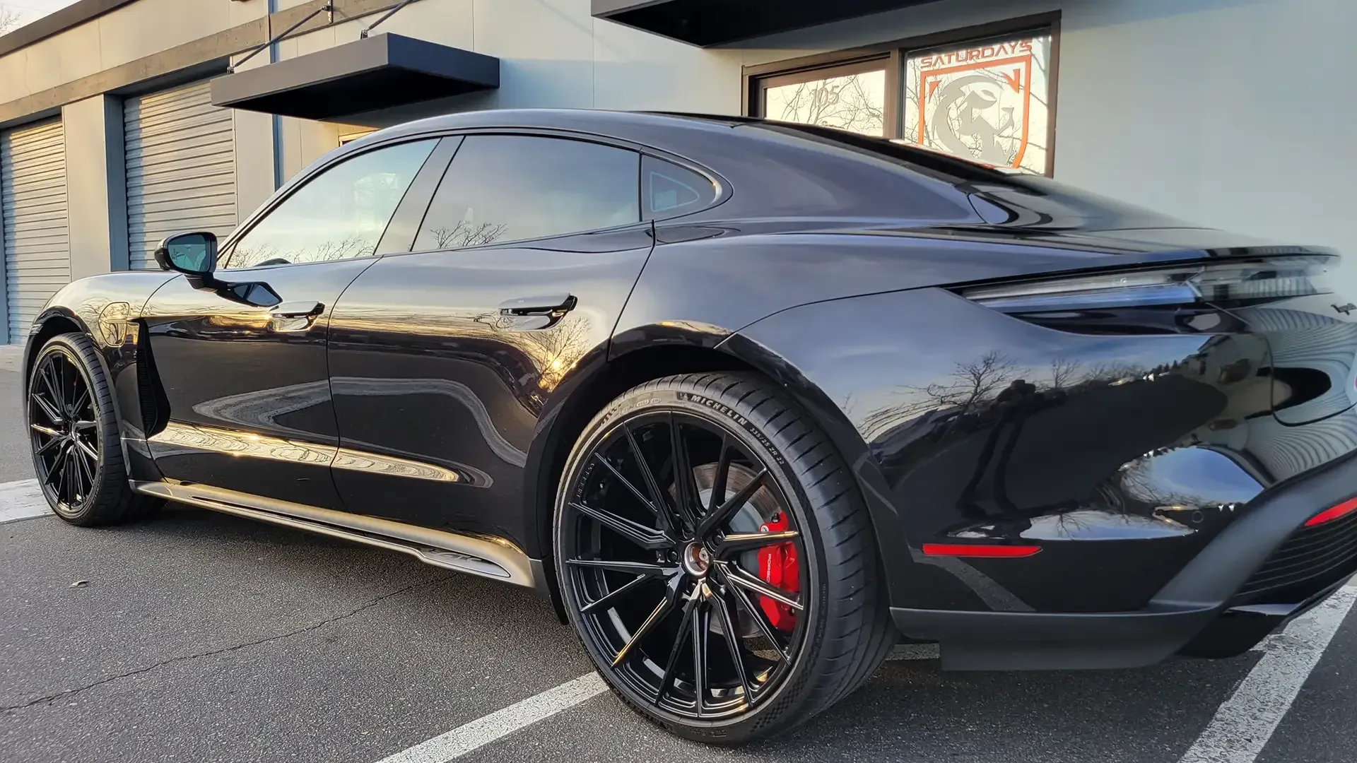 A black porsche taycan is parked in a parking lot in front of a building.