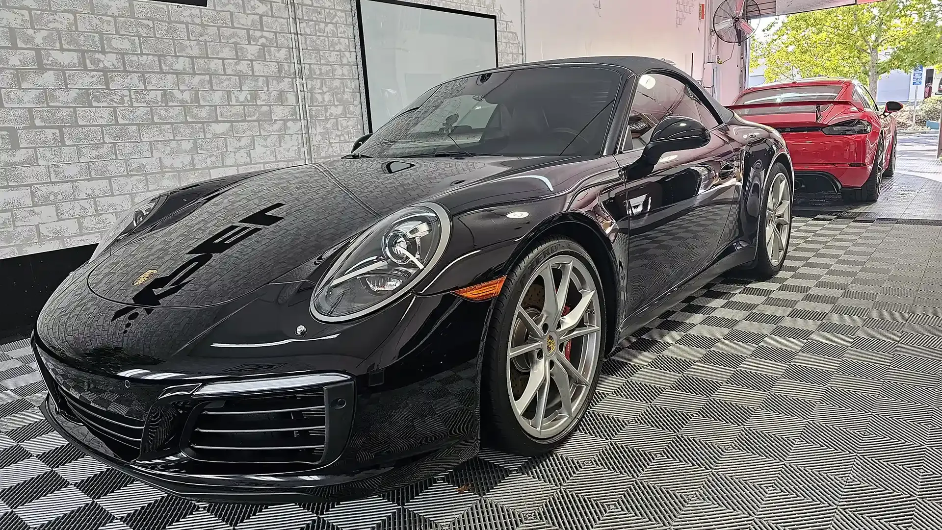 A black porsche 911 carrera is parked in front of a brick building.