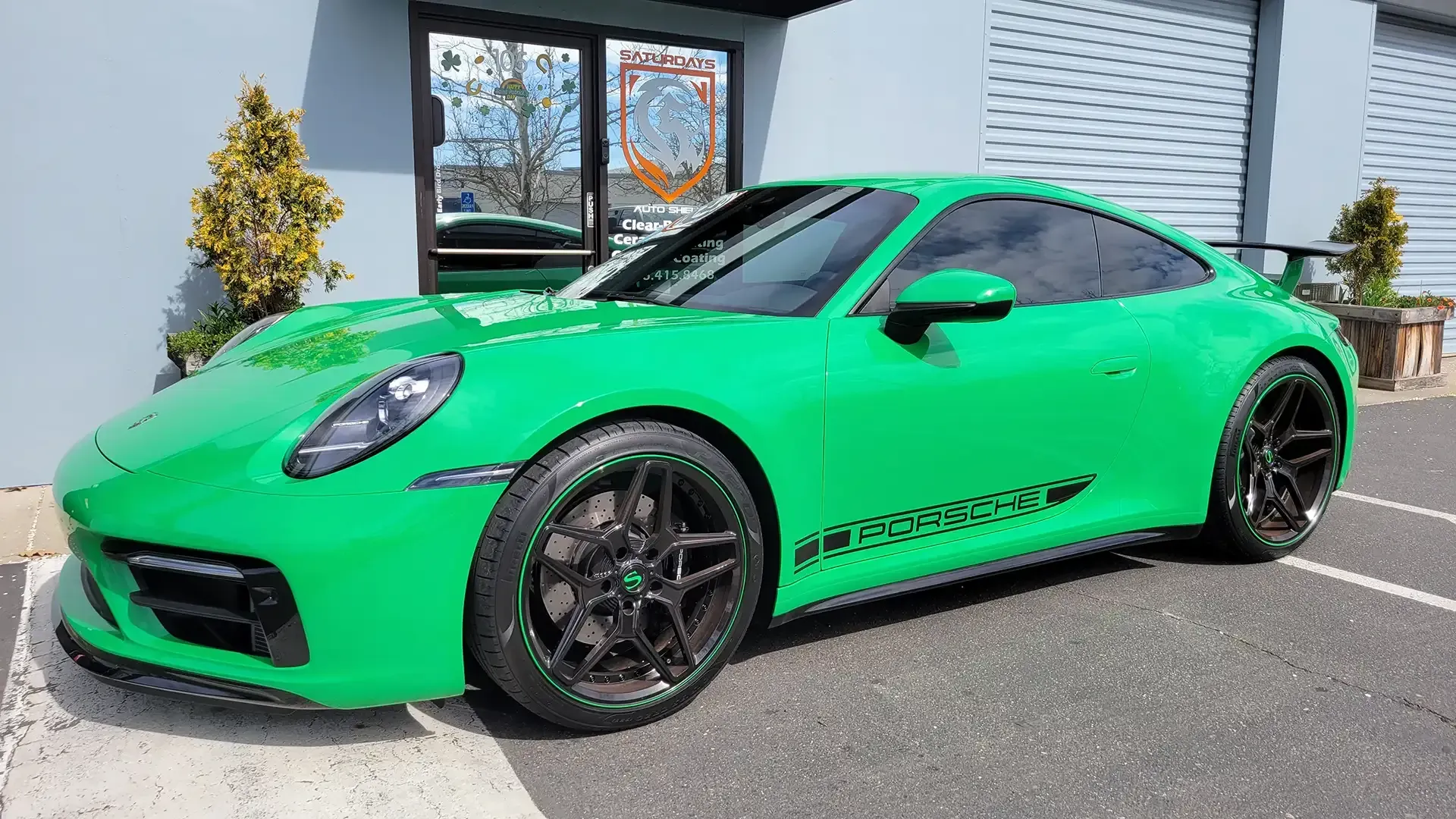 A green porsche 911 is parked in a parking lot in front of a building.