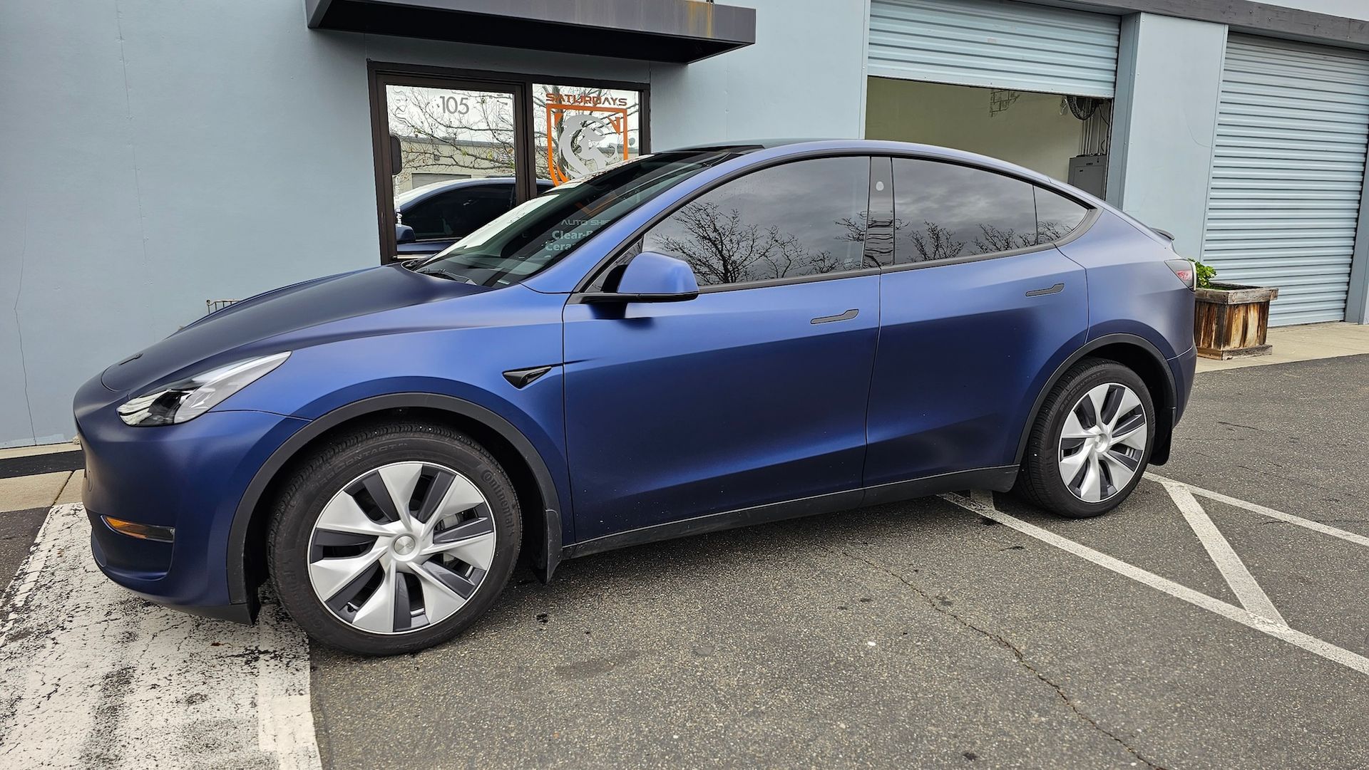 A blue tesla model y is parked in a parking lot in front of a building.