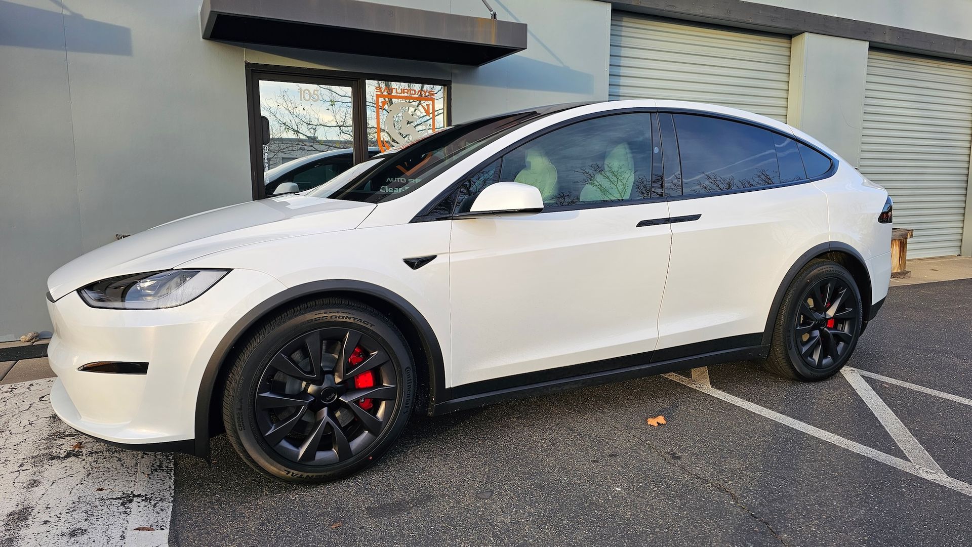 A white tesla model x is parked in a parking lot in front of a building.