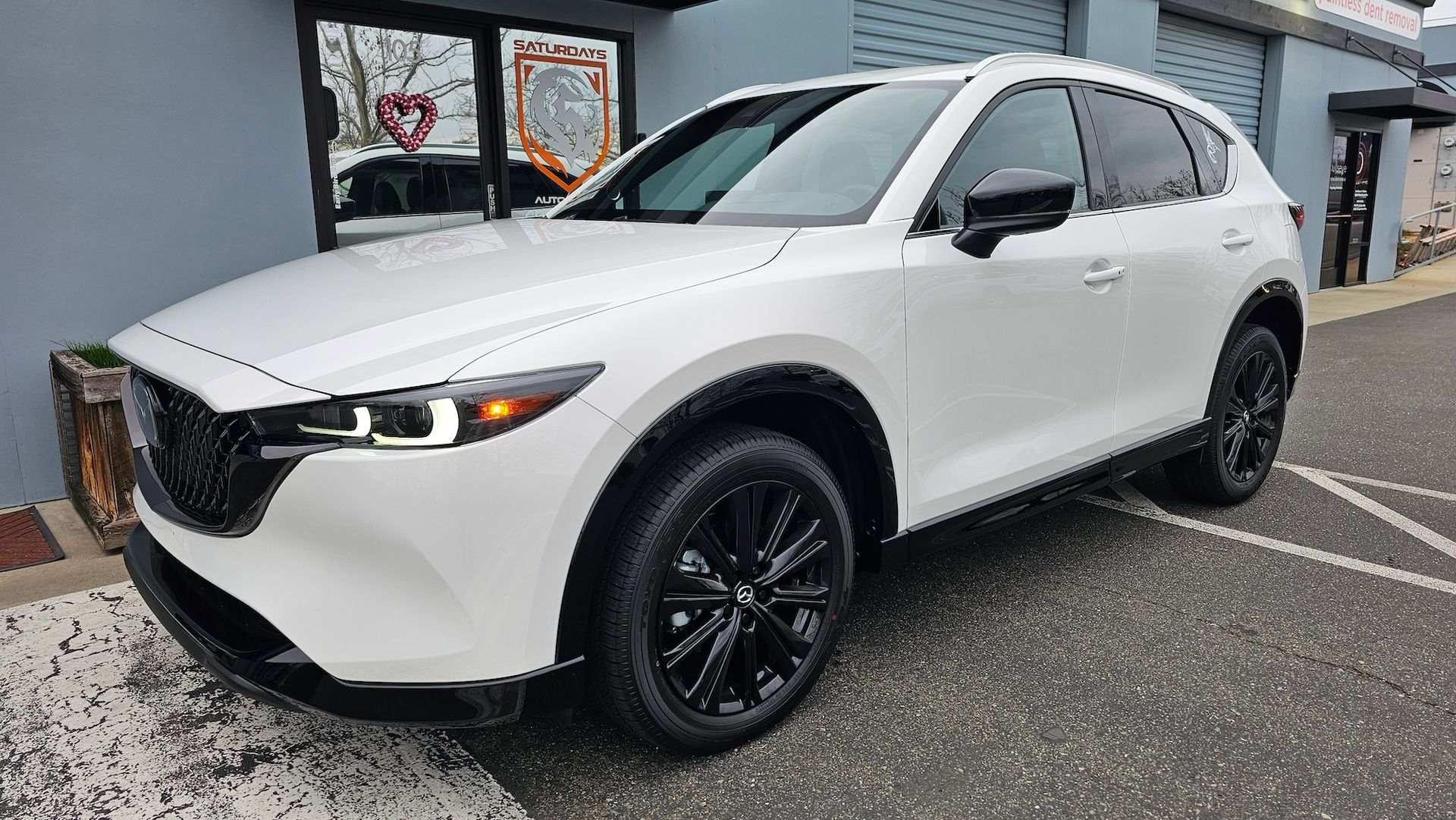 A white mazda cx-5 is parked in a parking lot in front of a building.