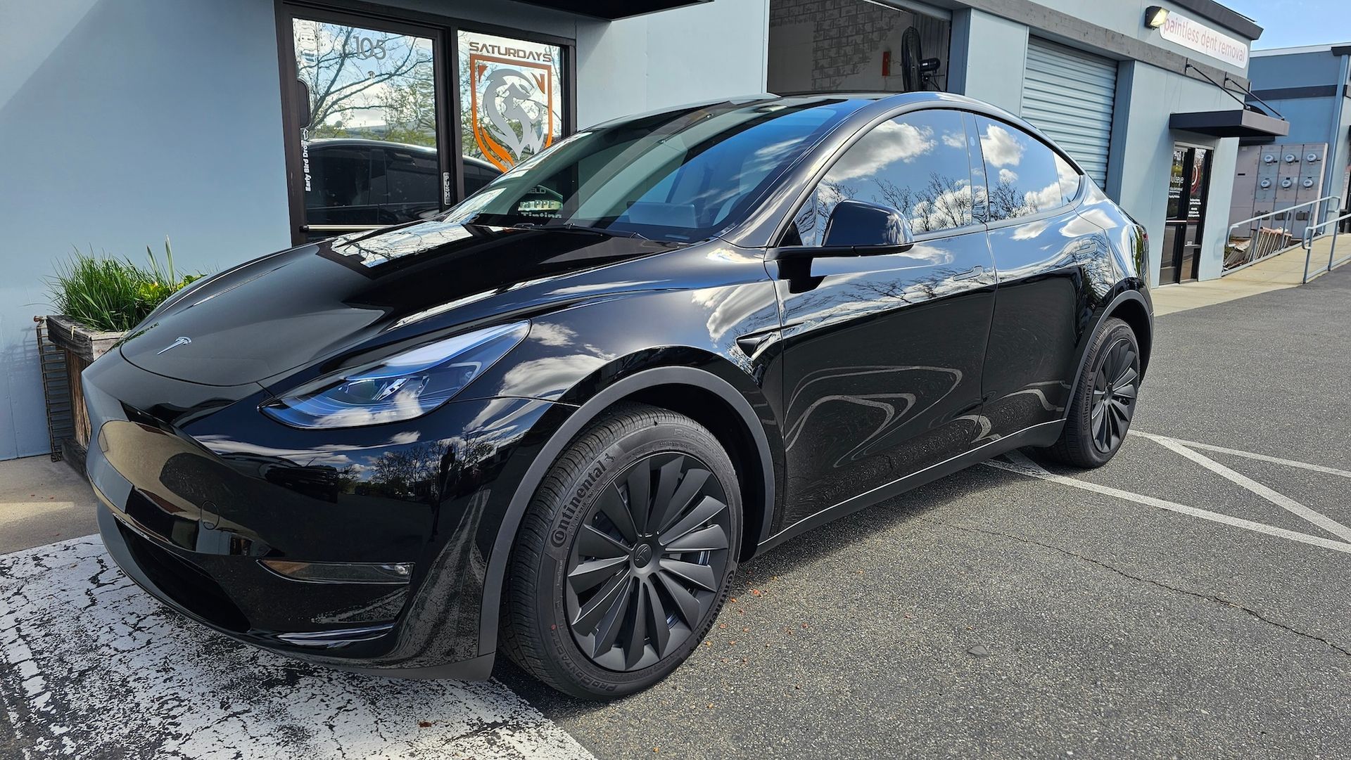 A black tesla model y is parked in a parking lot in front of a building.