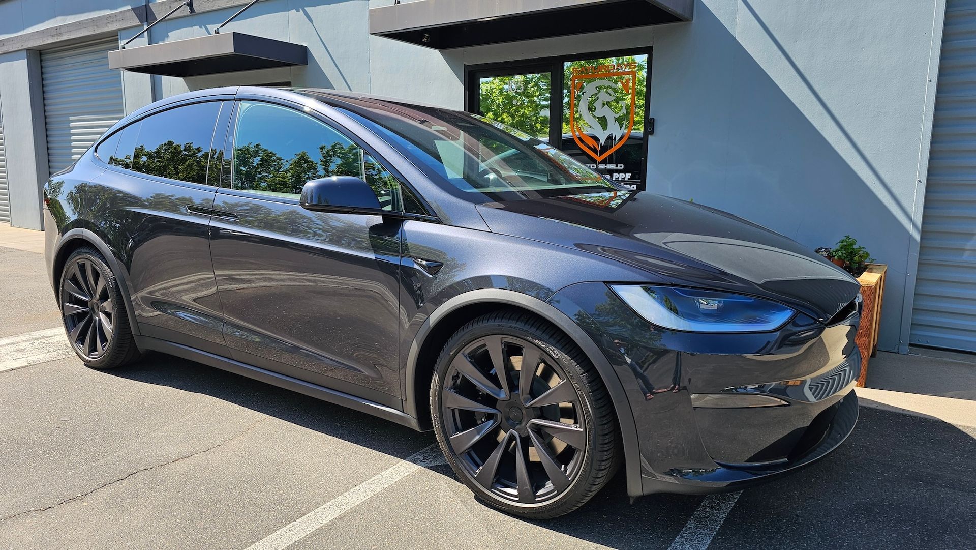 A black tesla model x is parked in a parking lot in front of a building.