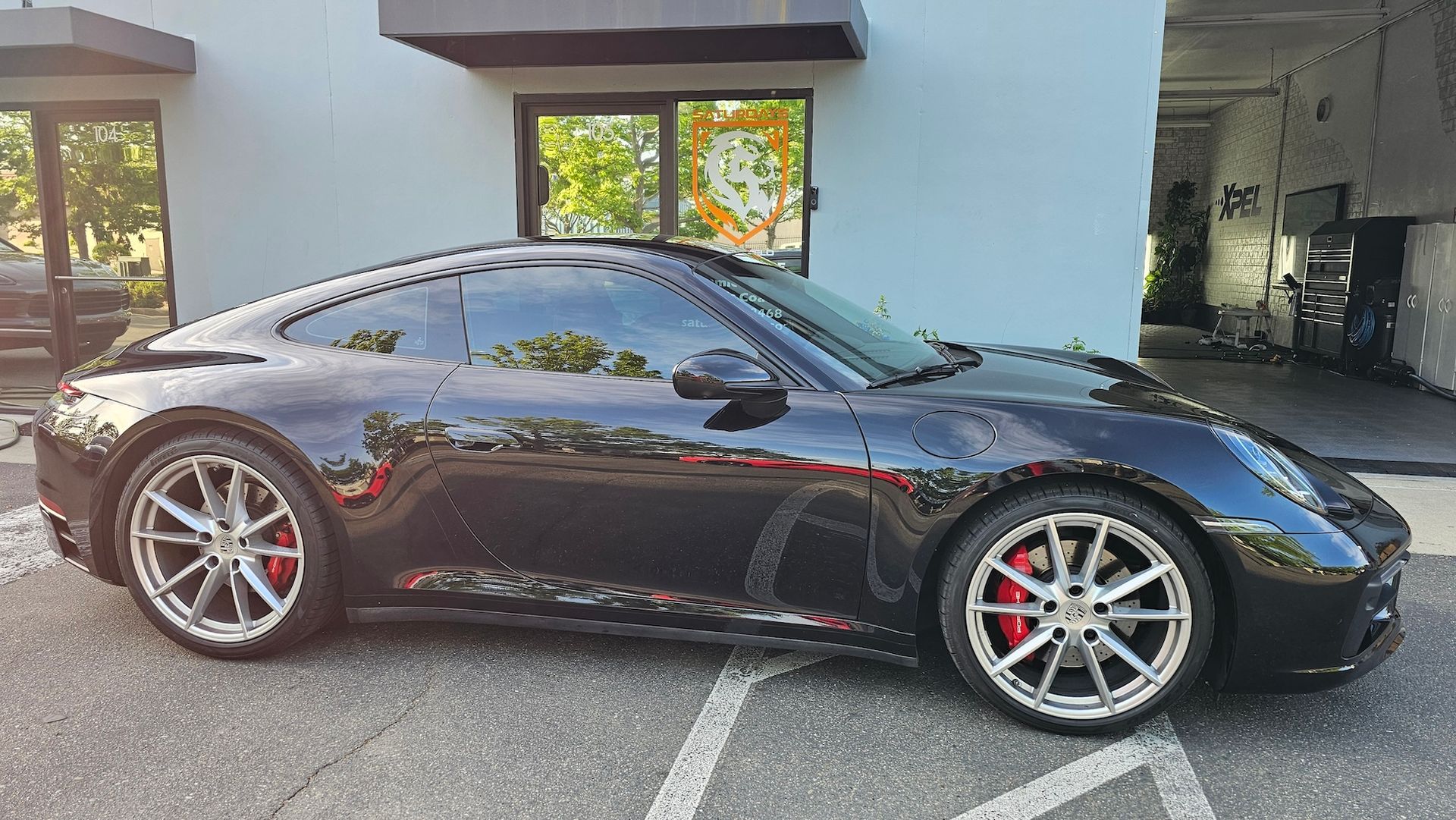 A black porsche 911 is parked in a parking lot in front of a building.
